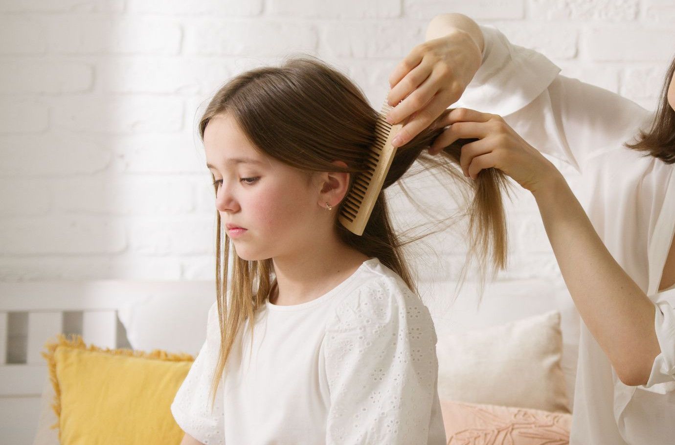 A mother carefully combs her daughter's hair in a warm and comfy indoor setting.