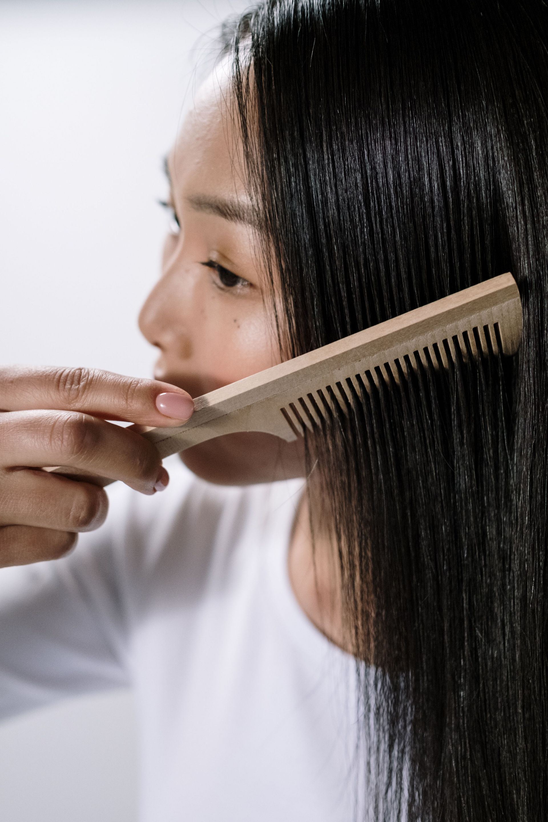 Close-up of an Asian woman using a wooden comb to style her hair indoors.