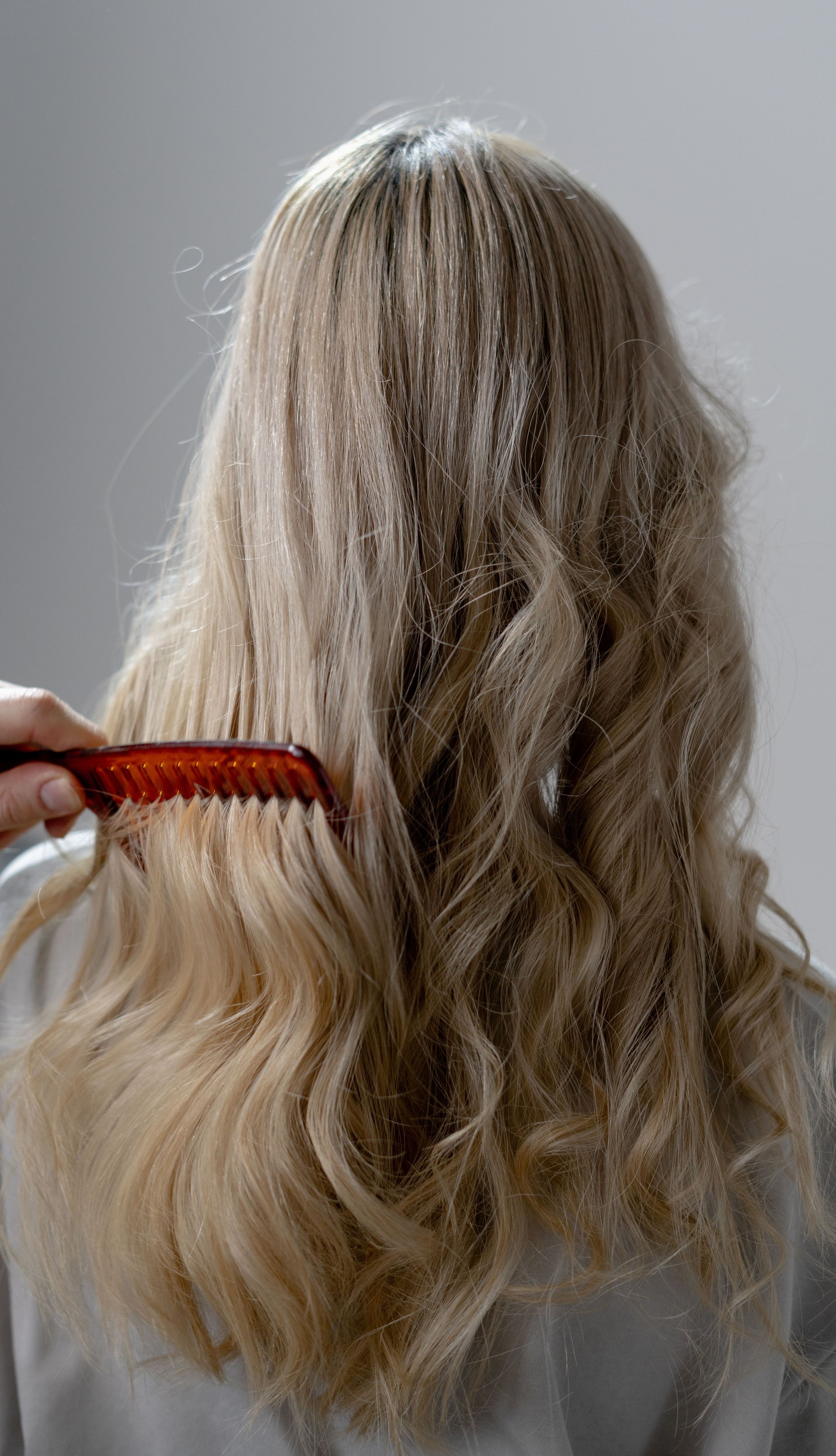 Back view of long blonde hair being combed into smooth curls with a red comb.